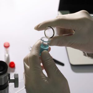 Gloved hands handling a vial with medical equipment in the background.